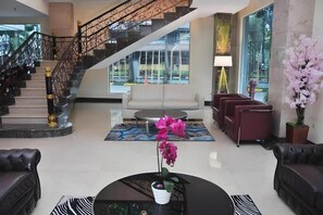 Un hall d’entrée avec un escalier, un canapé, une table basse et une orchidée en pot.