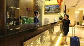 A hotel reception area with a glass partition, a reception desk, and a decorative wall with a painting.