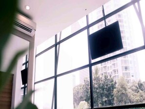 A room with large windows, a flat-screen TV mounted on the wall, and a ceiling air vent. - Casa Living Setiabudi Jakarta (Jakarta)