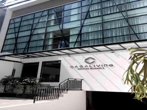 Un immeuble doté de grandes fenêtres en verre, une enseigne indiquant « CASALIVING, résidence avec services », et un escalier menant à l’entrée.