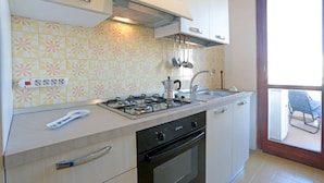 A compact kitchen with a gas stove, oven, and a sink. There is a window with a view of the outside. - Appartamento Calipso (Santa Croce Camerina)