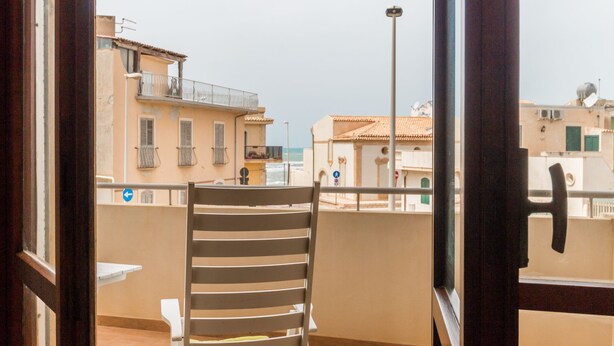 A balcony with a striped chair, a view of buildings, and a street lamp. - Appartamento Calipso (Santa Croce Camerina)