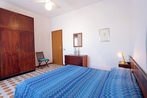 A bedroom with a bed, wooden wardrobe, chair, dresser, and a bedside lamp. - Appartamento Calipso (Santa Croce Camerina)