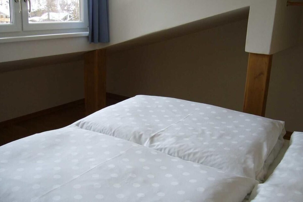 Un dormitorio con dos camas, una ventana con cortinas azules, y cabecera y paneles laterales de madera.