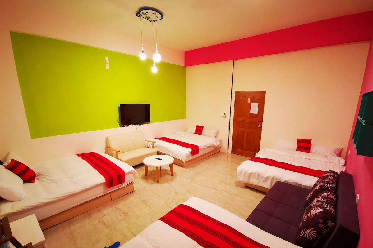 A hotel room with four beds, a sofa, a television, and a green accent wall.