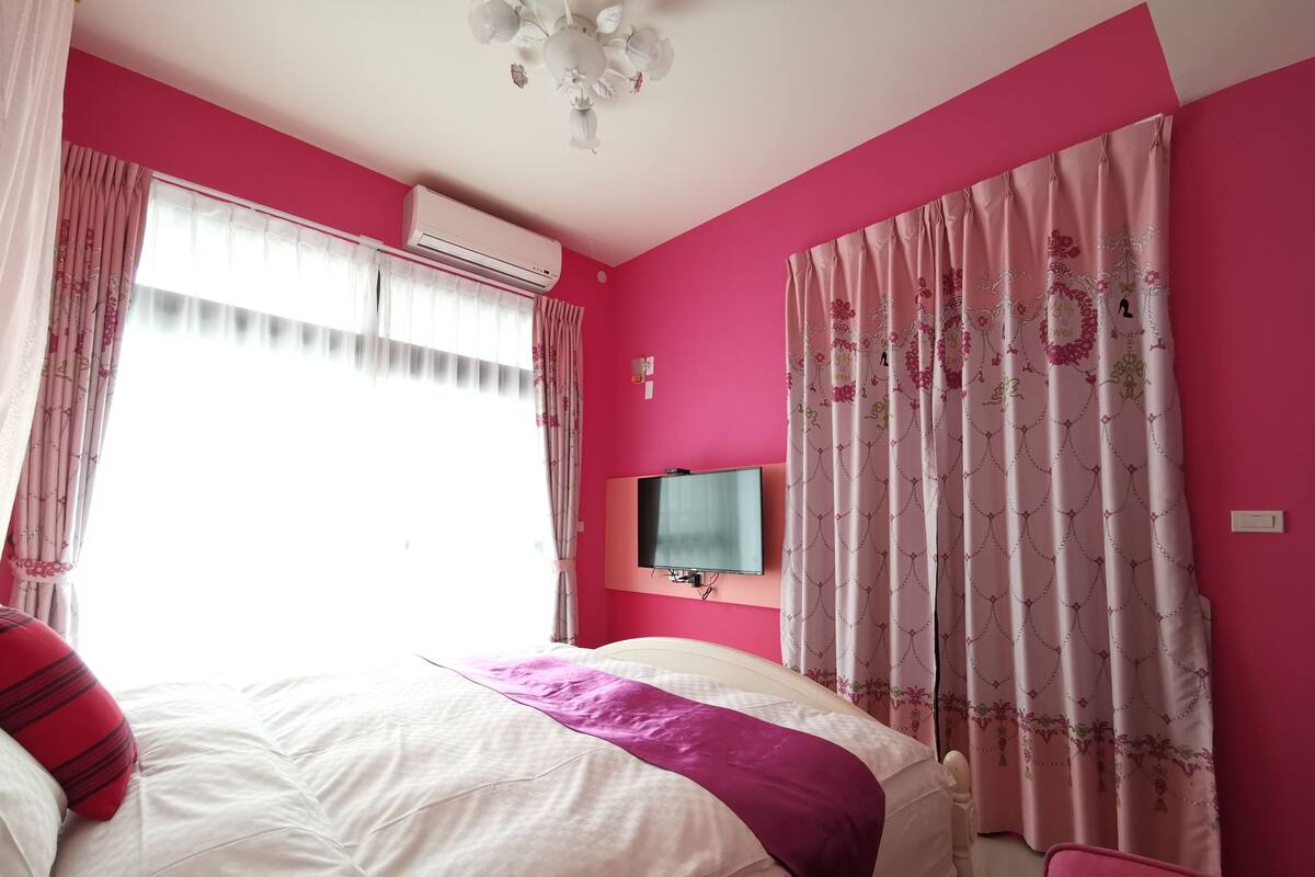 A bedroom with a bed, a TV, and pink walls.
