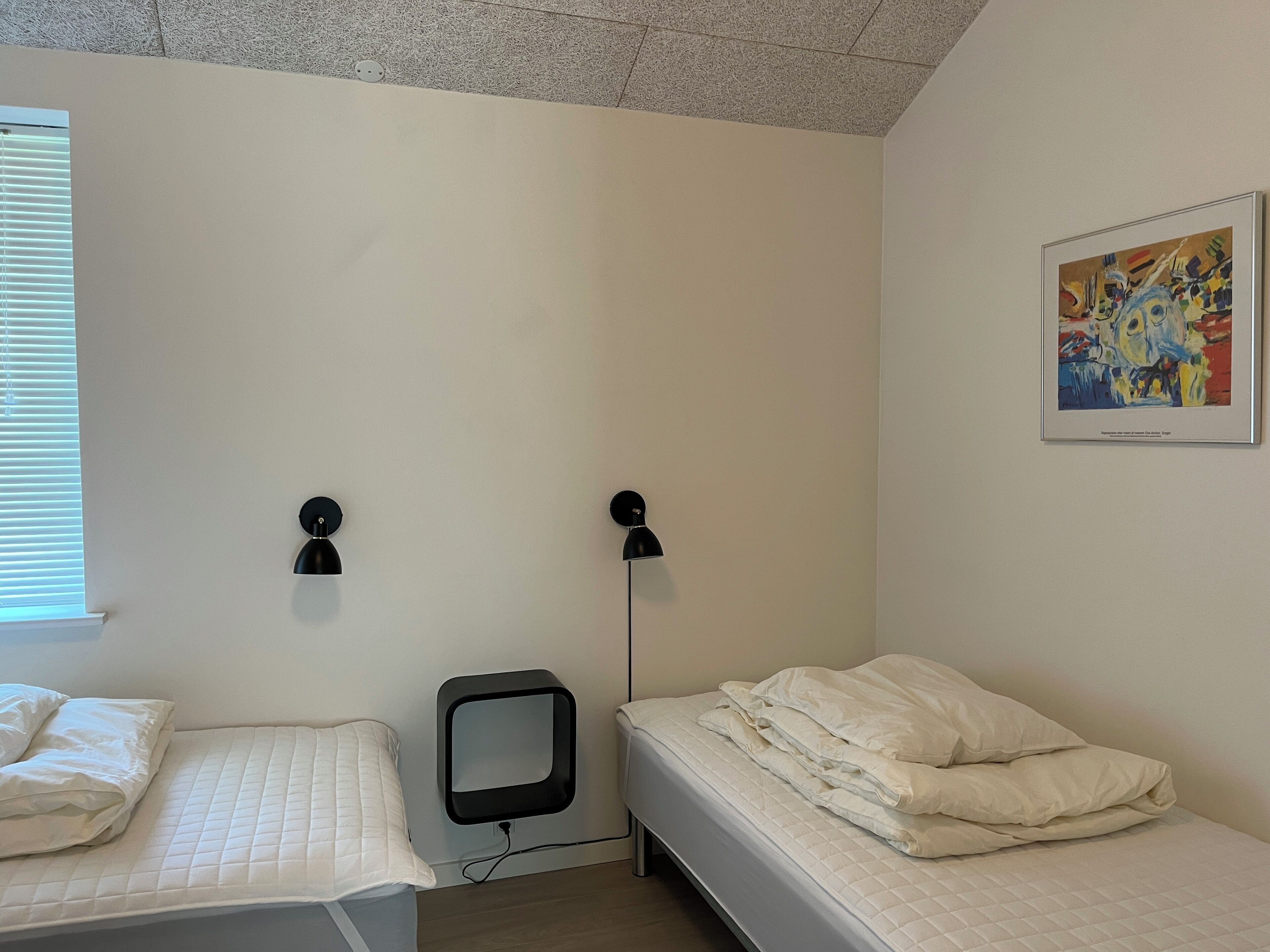 A small, clean room with two beds, a wall-mounted TV, and a painting.