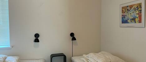Une petite chambre propre, avec deux lits, un téléviseur fixé au mur et un tableau.