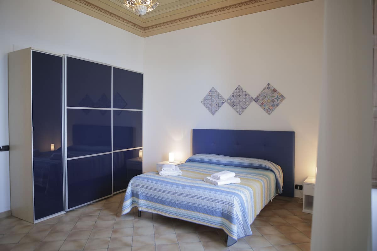 Une chambre dotée d’une grande armoire, d’un lit avec une literie à rayures et d’œuvres d’art décoratives accrochées au mur.