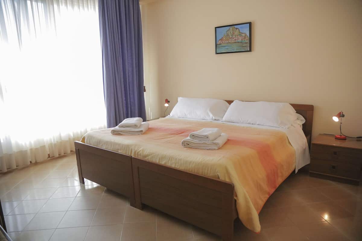 A neatly made bed with pillows and folded towels, a bedside table with a lamp, and a painting on the wall.