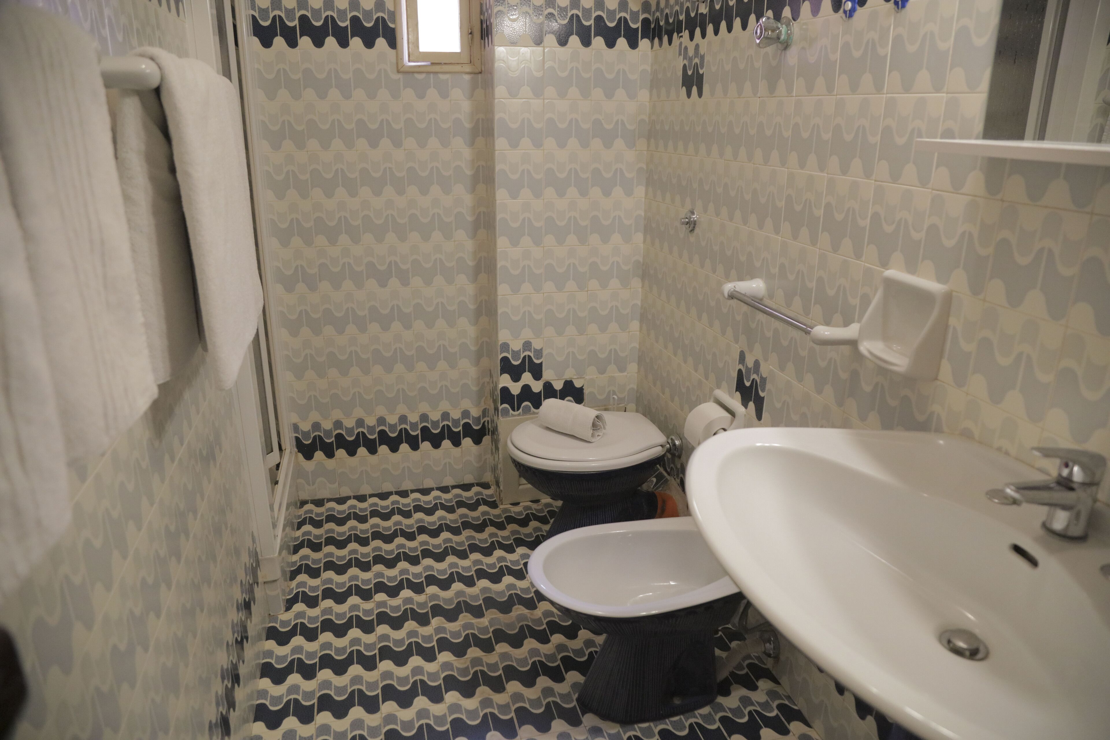 Et badeværelse med mønstrede fliser, toilet, bidet og håndvask.