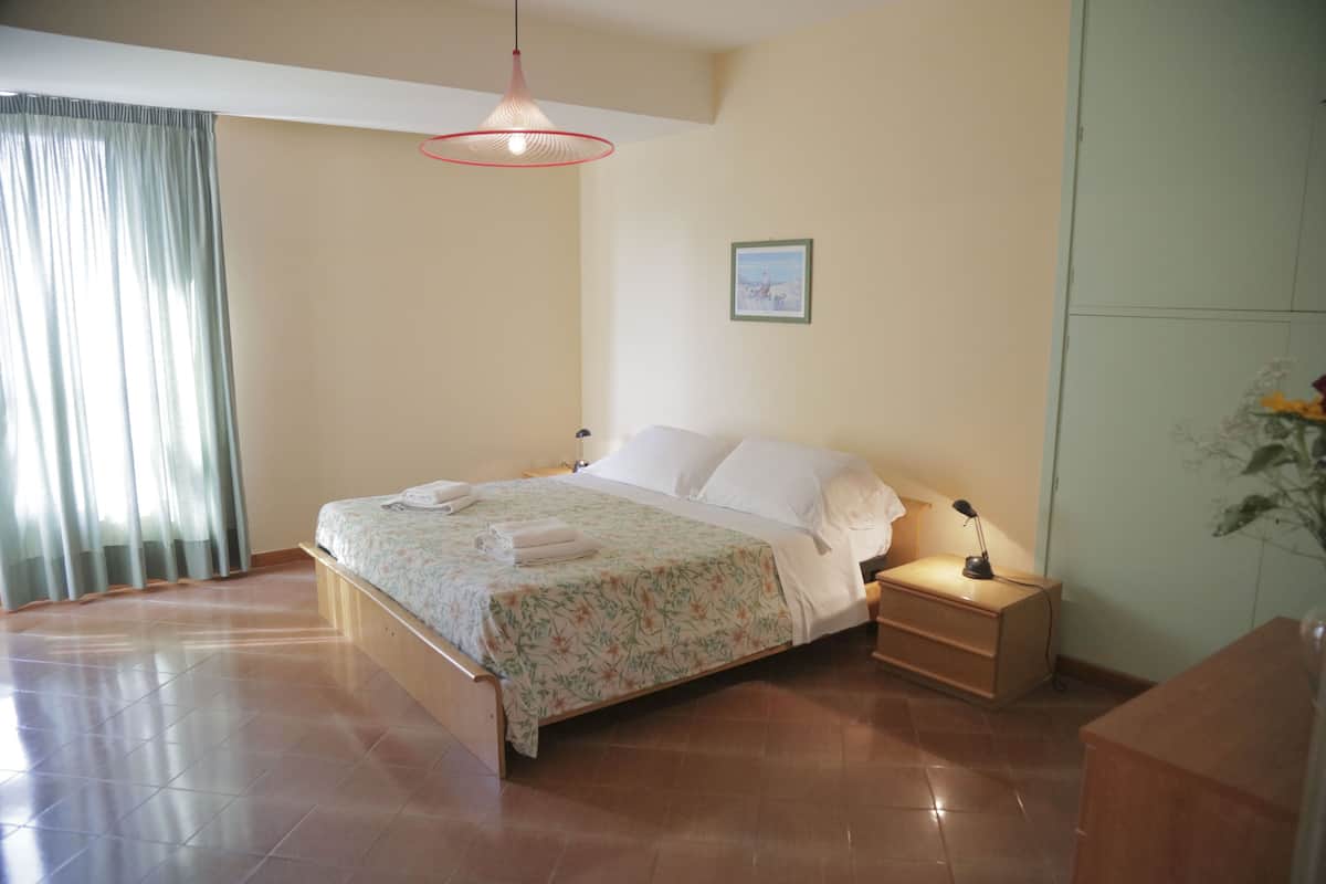 A neatly made bed with a floral bedspread and white pillows, a bedside table with a lamp, and a framed picture on the wall.