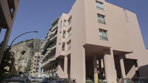 Un edificio de varios pisos con balcones, un estacionamiento y una montaña al fondo.