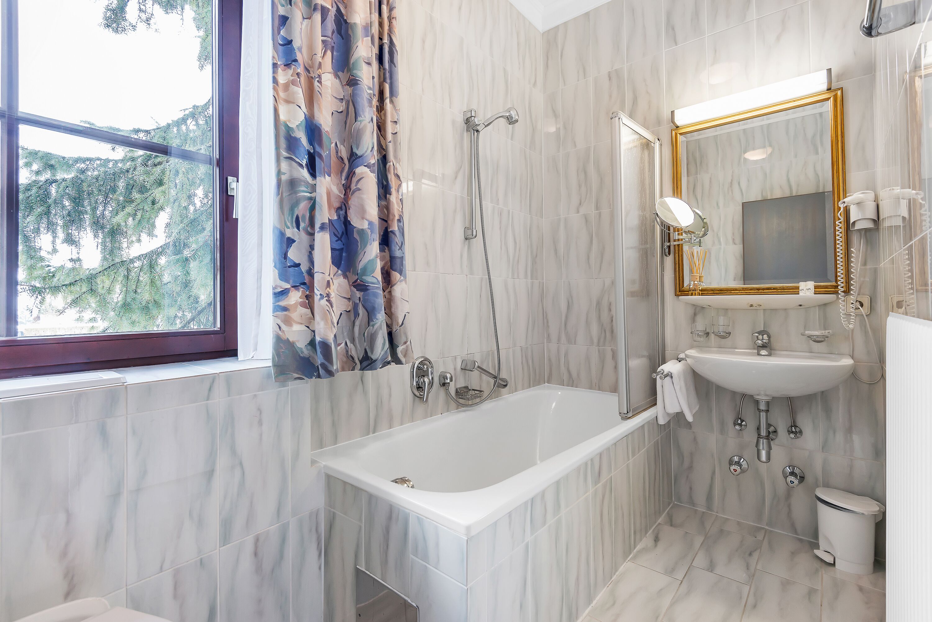 Une salle de bain moderne avec une baignoire, une douche et un lavabo, des murs en marbre et une fenêtre avec des rideaux.