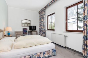 Un dormitorio con cama, cómoda, televisor, ventana con cortinas y radiador.