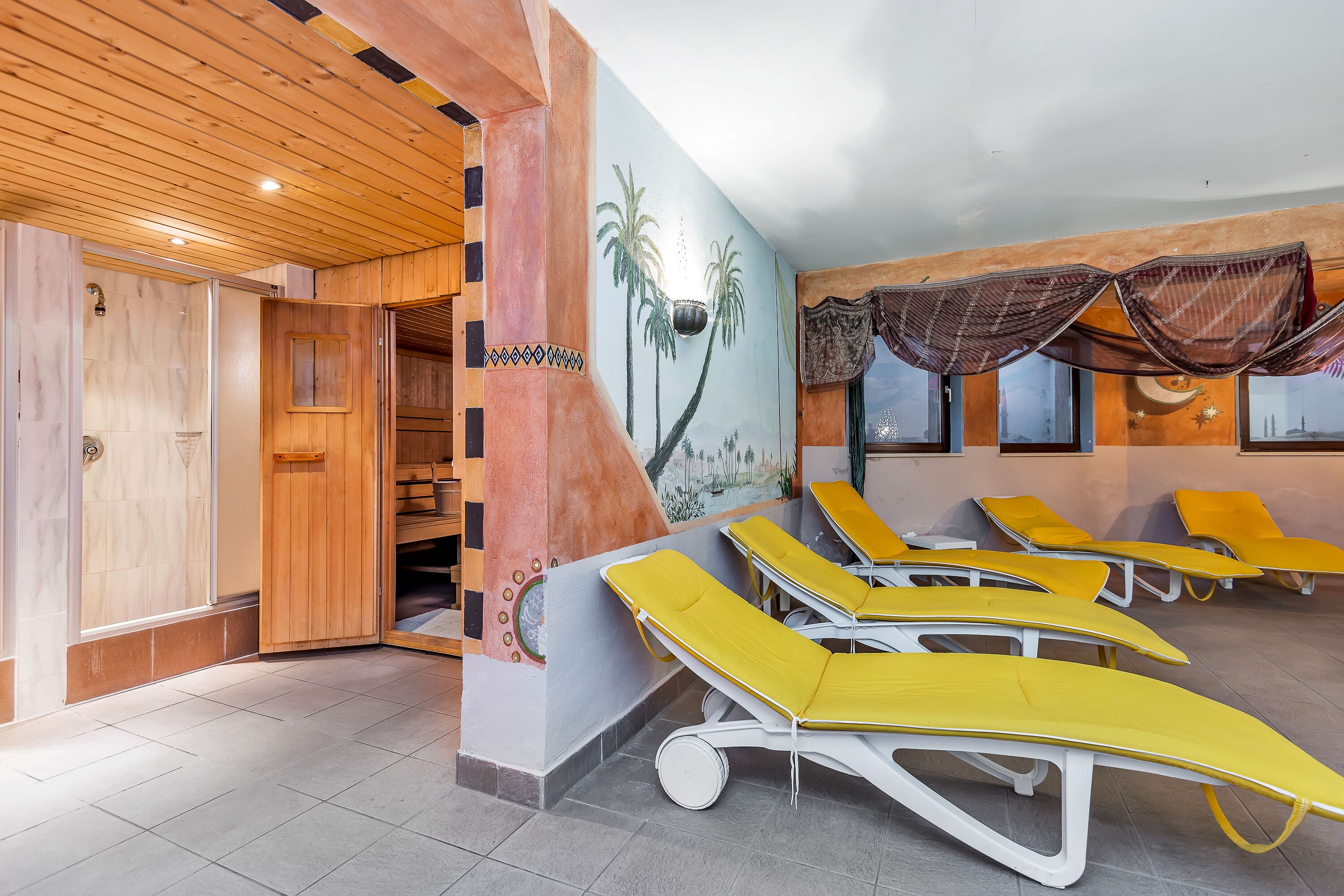 A room with wooden ceiling, a mural of palm trees, and yellow sun loungers.