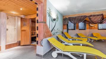 A room with wooden ceiling, a mural of palm trees, and yellow sun loungers.