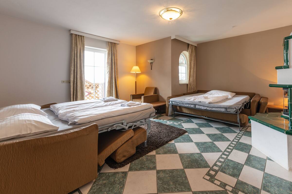 Una camera d'albergo con due letti, una scrivania, una sedia, una lampada e una finestra con tende.