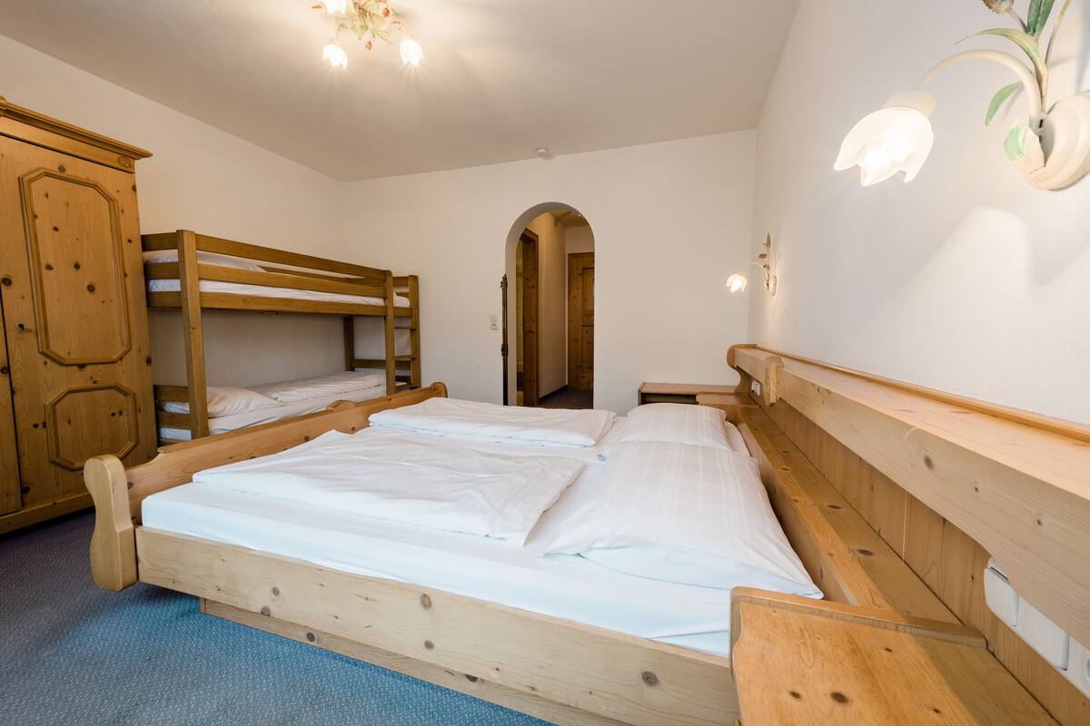 Una stanza con tre letti a castello in legno, un'armadietto in legno e un comodino.