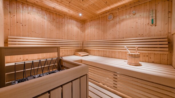A wooden sauna with benches and a wooden bucket. - Hotel Rothirsch by Skinetworks (Sankt Johann im Pongau)