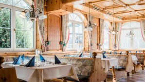 A restaurant with wooden interiors, tables set with blue napkins, and large windows. - Hotel Rothirsch by Skinetworks (Sankt Johann im Pongau)