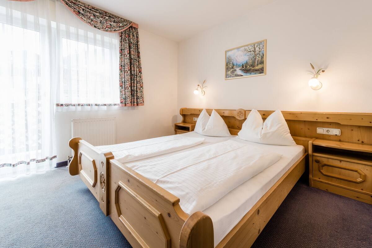 Un letto in legno con lenzuola bianche, un comodino e una lampada fissata al muro.