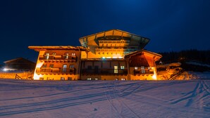 Um hotel de vários andares com uma varanda saliente no segundo andar, situado em uma paisagem nevada à noite.