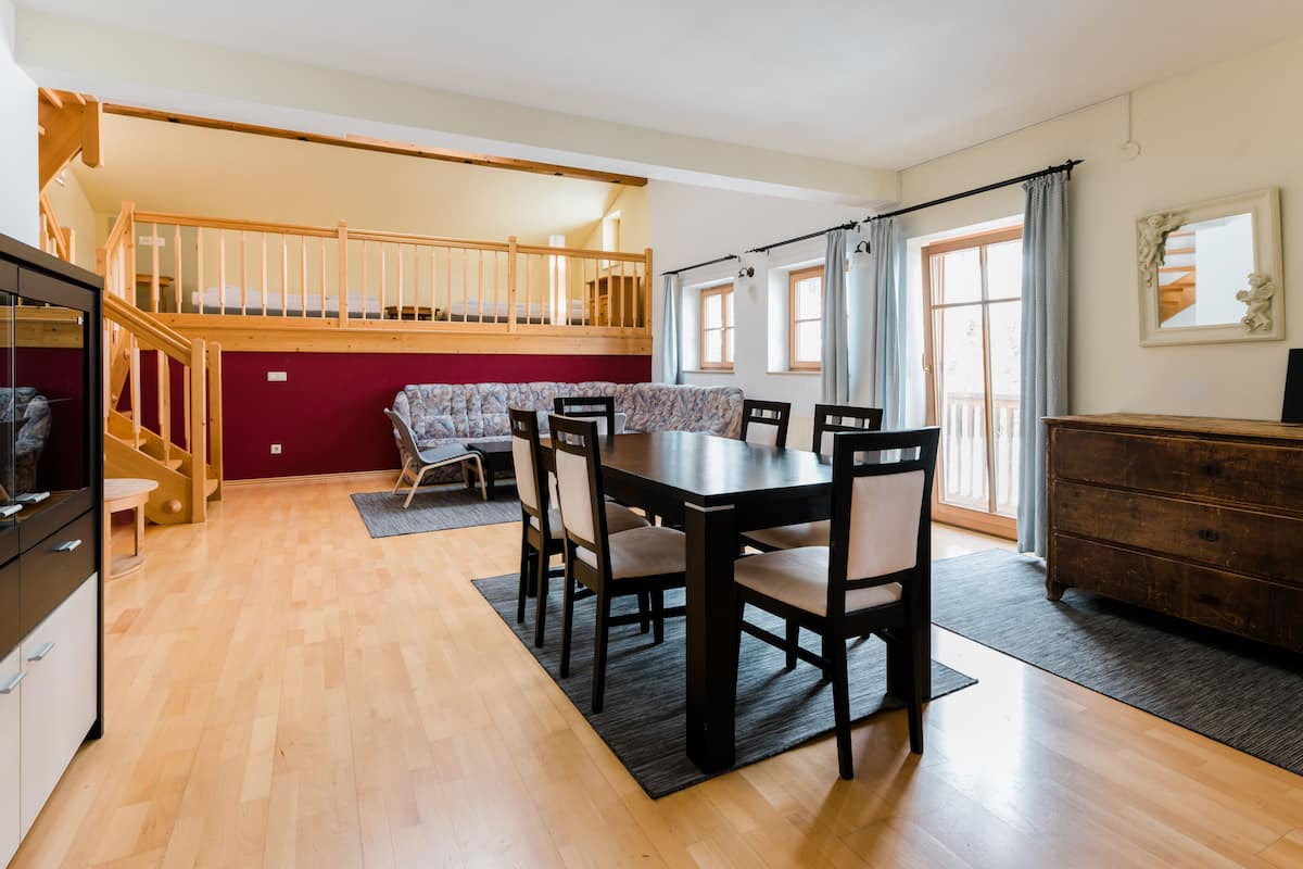Un comedor amplio con una mesa y sillas de madera, una escalera que lleva a un nivel superior y vistas al exterior a través de grandes ventanales.