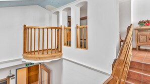 Um quarto com uma cadeira de madeira, uma janela pequena e uma escada.