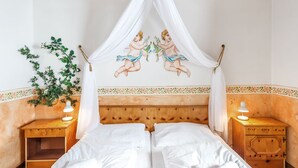 Quarto com teto de madeira, cama de dossel, duas mesas de cabeceira com abajures e um ornamento floral na parede.