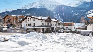 Une rue enneigée bordée de bâtiments traditionnels en bois, un ciel dégagé et des montagnes enneigées en arrière-plan.