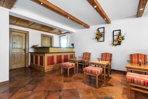 A spacious room with a wooden bar, red cushioned chairs, and a tiled floor. - Appartements Traxl by Skinetworks (Sankt Anton am Arlberg)