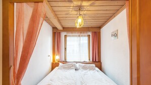 Une pièce avec un lit, un plafond en bois et une fenêtre avec des rideaux.