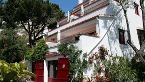 A white building with red doors and a stone-paved courtyard. - 2 -Spectacular apartment with sea view, large terrace, 4 min. walk to the beach (Roses)