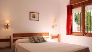 Een slaapkamer met een houten hoofdbord, een enkel bed met een gestreept kussen, twee bedlampen en een raam met rode gordijnen.