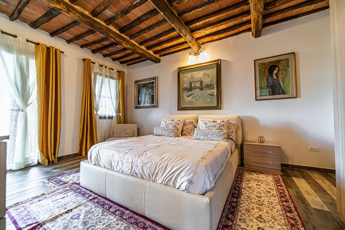 Una camera da letto con soffitto in legno, un letto grande con molti cuscini, un comodino e un quadro appeso al muro.