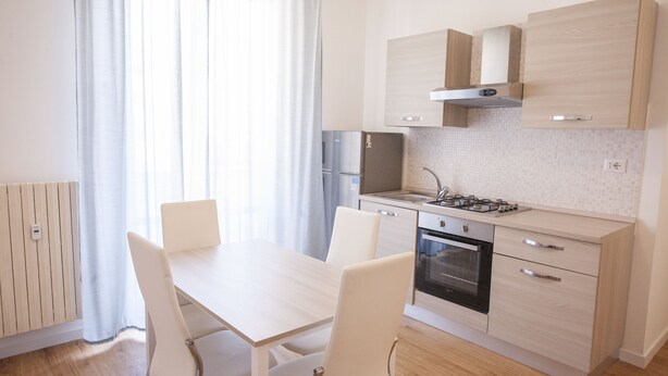 A modern kitchen with a dining table and chairs, a built-in oven, and a refrigerator. - Appartamenti Le Maree (Portoferraio)