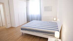 A bedroom with a bed, a nightstand, a wardrobe, and a window with curtains. - Appartamenti Le Maree (Portoferraio)
