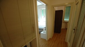 A hallway with a wooden floor, a white door, and a window with blinds. - Appartamenti Le Maree (Portoferraio)