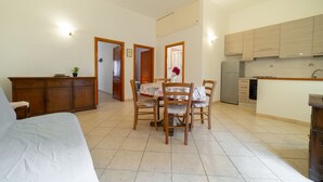 Un vaste espace de vie comprenant une table à manger et des chaises, un canapé, une cuisine avec des meubles en bois et un sol carrelé.