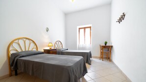 Une chambre avec deux lits, une table de chevet, une chaise, une petite table avec une plante et une fenêtre avec des rideaux.