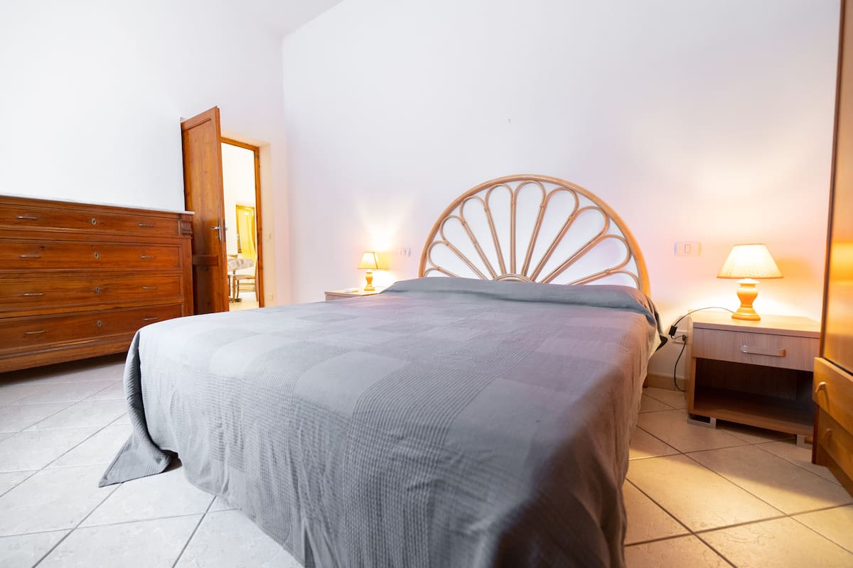Une chambre à coucher comprenant un lit, une commode en bois, des tables de chevet avec des lampes et une porte donnant sur une autre pièce.