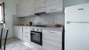 Une cuisine moderne avec des meubles gris, un four encastré, une cuisinière à gaz et un réfrigérateur blanc.