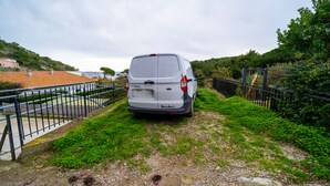 Un fourgon blanc était garé sur un chemin bordé d’herbe, avec une clôture métallique d’un côté et une zone pavée avec des bâtiments de l’autre.