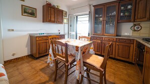 A kitchen with wooden cabinets, a dining table with chairs, and a window with curtains. - Bilocale La Terrazza sul Mare (Campo nell'Elba)