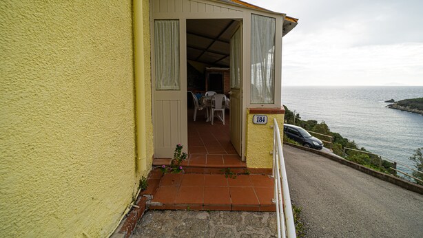 A yellow building with a balcony, a number 184 sign, and a view of the sea. - Bilocale La Terrazza sul Mare (Campo nell'Elba)
