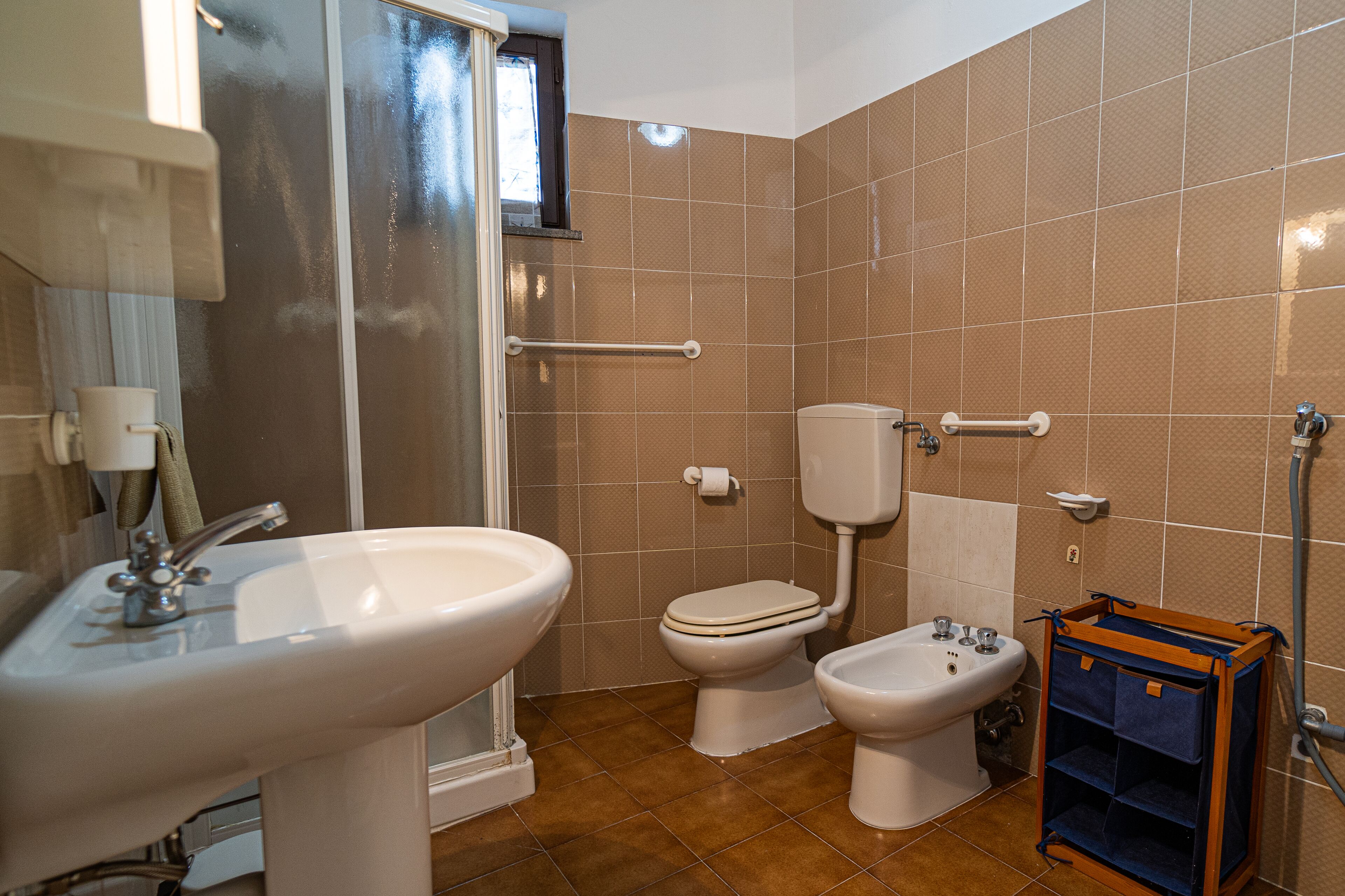A bathroom with a sink, toilet, bidet, and a small wooden cabinet.