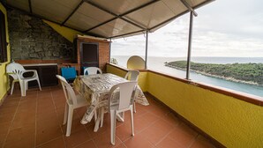 A covered outdoor patio with a table and chairs, a grill, and a view of the sea. - Bilocale La Terrazza sul Mare (Campo nell'Elba)