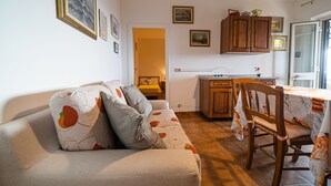A cozy living room with a sofa, a dining table with a chair, wooden cabinets, and a kitchen area. - Bilocale La Terrazza sul Mare (Campo nell'Elba)