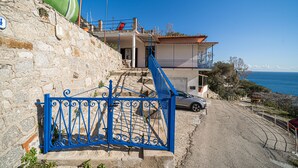 A coastal property with a stone wall, a blue gate, and a car parked in front. - Casa Fetovaia (Campo nell'Elba)